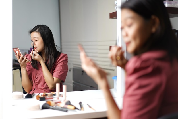 화장대 거울 앞에서 화장을 하고 있는 아름다운 아시아 여성