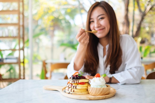 A beautiful asian woman eating ice cream and a mixed berries pancakes with whipped cream by wooden spoon