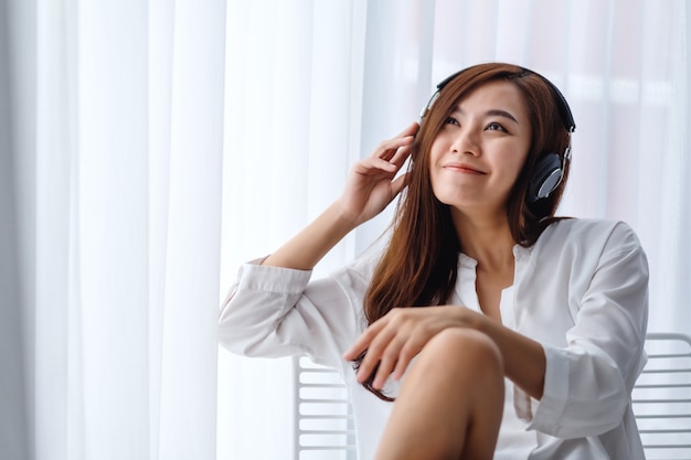 A beautiful asian woman enjoy listening to music with headphone in bedroom , happiness and relaxation concepts