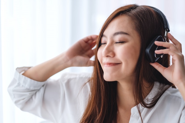 A beautiful asian woman enjoy listening to music with headphone in bedroom , happiness and relaxation concepts
