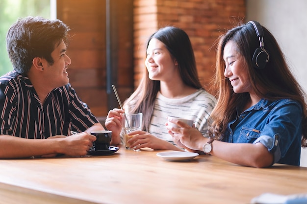 Una bella donna asiatica si diverte ad ascoltare musica con le cuffie mentre beve caffè con gli amici