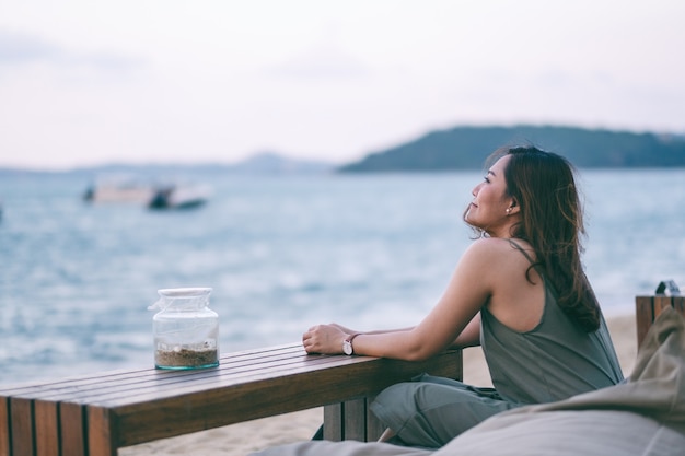 美しいアジアの女性は海岸沿いのビーチに座って楽しむ