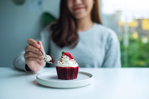 美しいアジアの女性は赤いベルベットのカップケーキを食べて楽しんだ