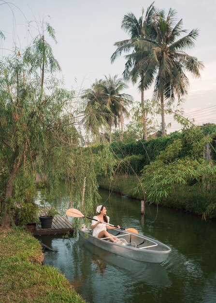 Photo beautiful asian woman enjoying paddling on transparent boat at canal in tropical forest on weekend