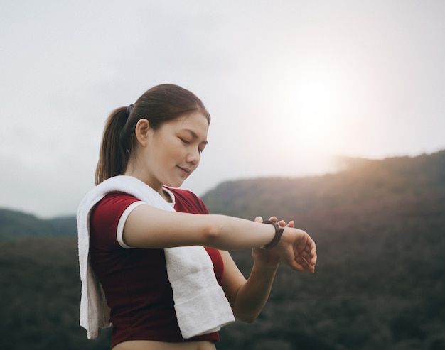 Beautiful asian woman exercises outside and looks her smart watch