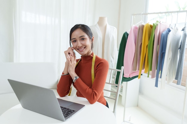 Beautiful asian woman fashion designer sitting in the clothing store and studio In front of the camera to recording vlog video live streamingBusiness online influencer on social media concept