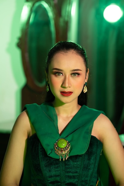 A beautiful Asian woman in a green dress has a very exotic face with ear and body jewelry while