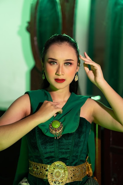 A beautiful Asian woman in a green dress is posing with her hands very gracefully and has green eyes