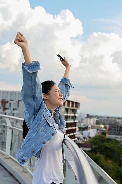 Beautiful Asian woman hands up in the air standing on the rooftop of the building freedom carefree