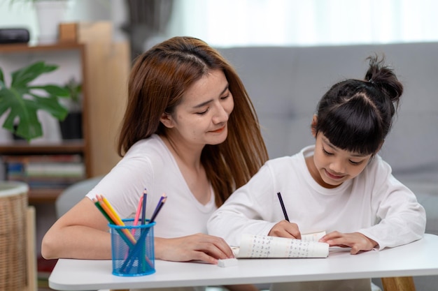 Bella donna asiatica che aiuta sua figlia a fare i compiti a casa.