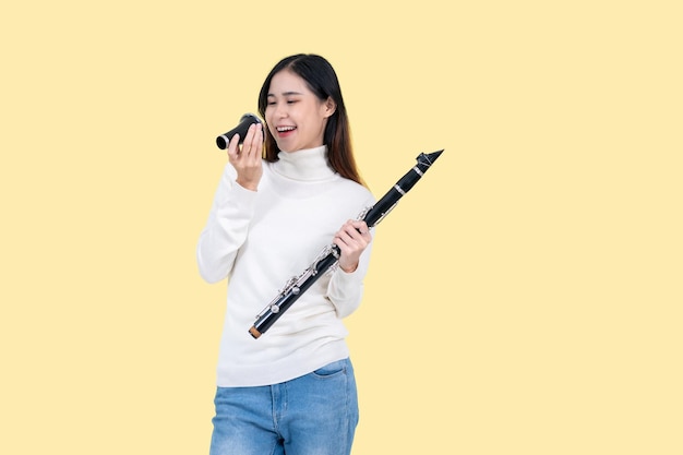 A beautiful Asian woman holding a clarinet while standing against an isolated yellow background