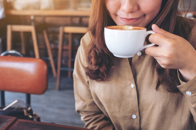 Una bella donna asiatica che tiene e beve caffè caldo con sentirsi bene nella caffetteria