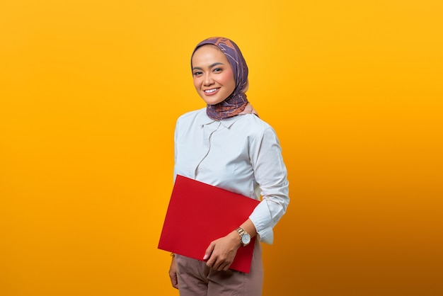 Beautiful Asian woman holding folders while looking at camera with smiling face on yellow background