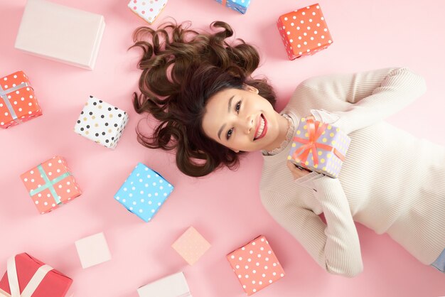Beautiful asian woman holding a gift box and lying on pink