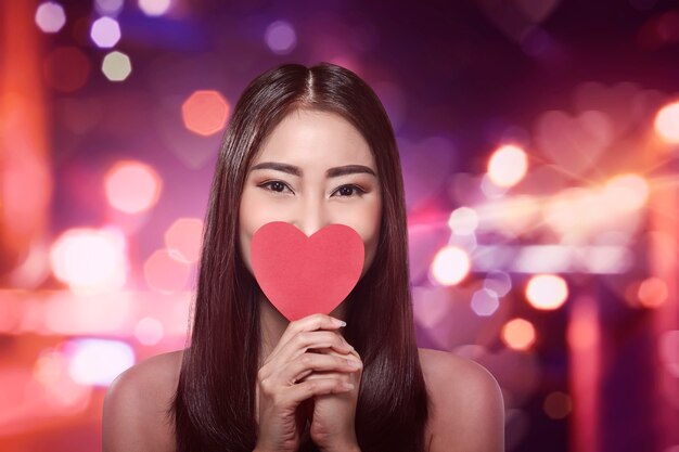 Photo beautiful asian woman holding a red heart