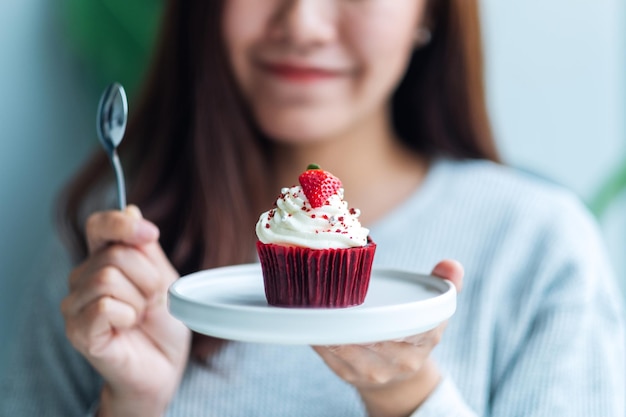 赤いベルベットのカップケーキとスプーンを持っている美しいアジアの女性