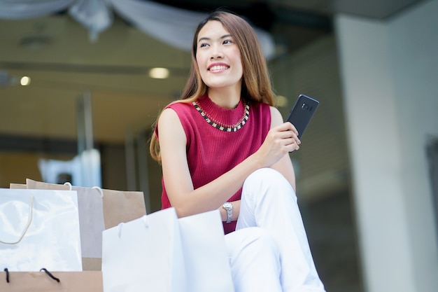 Foto bella donna asiatica che tiene smartphone e seduto con le borse