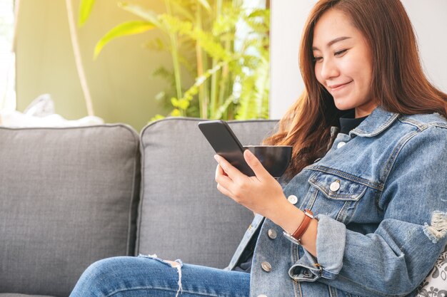 Bella donna asiatica che tiene e utilizzando smart phone mentre beve il caffè