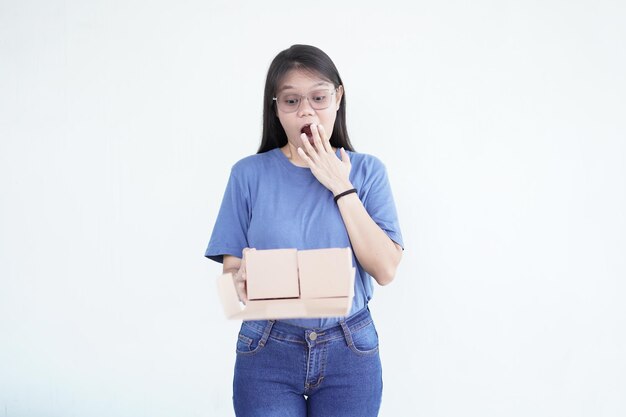 美しいアジア人女性が箱のパッケージを持ち白い背景にショックを受けたワウの表情を示しています