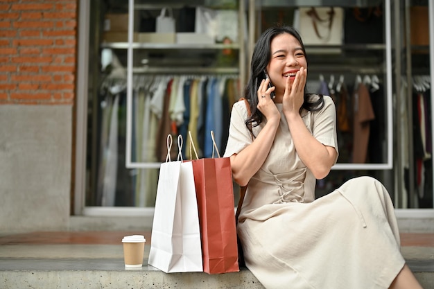 아름다운 아시아 여성이 계단에 앉아 전화 통화를 즐기고 있습니다.