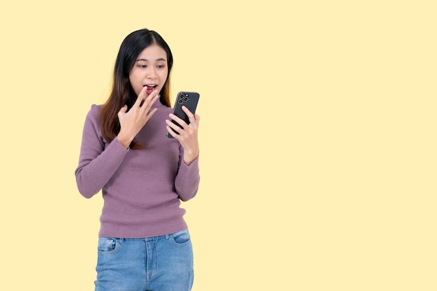 한 아름다운 아시아 여성이 충격과 놀란 얼굴로 스마트폰 화면을 보고 있다