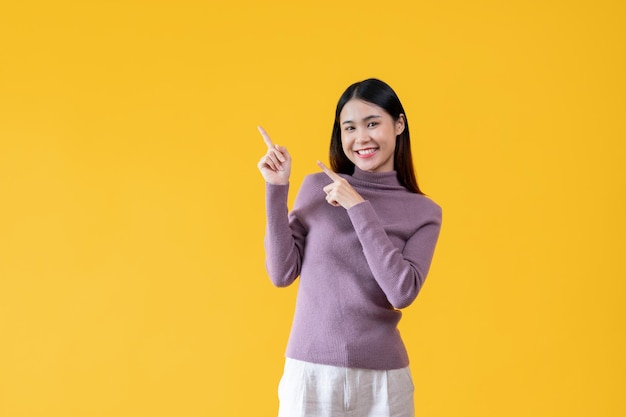 A beautiful Asian woman is smiling and pointing her fingers up at an empty space isolated