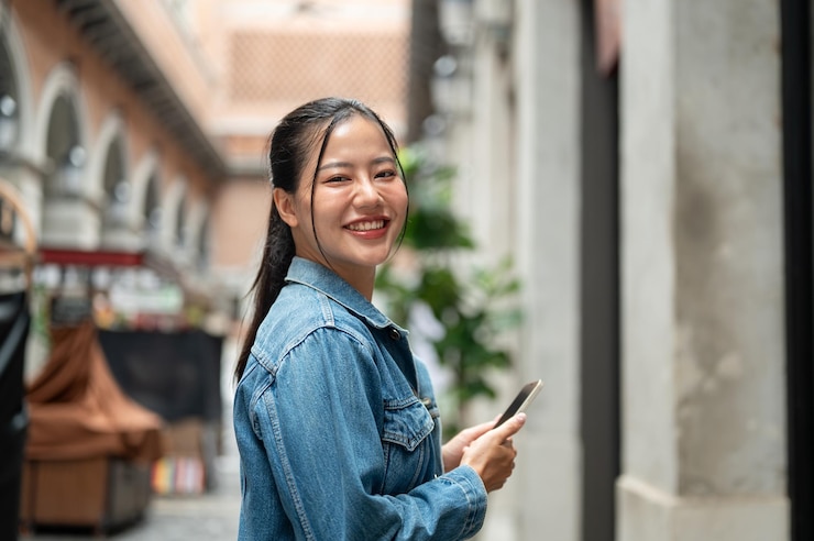 Photo 一位美麗的亞洲女人站在室外,拿著智能手機向相機微笑