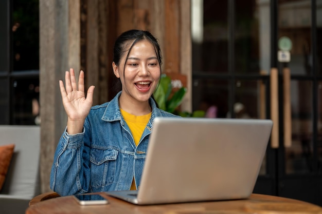 A beautiful Asian woman is waving her hand during an online meeting on her laptop