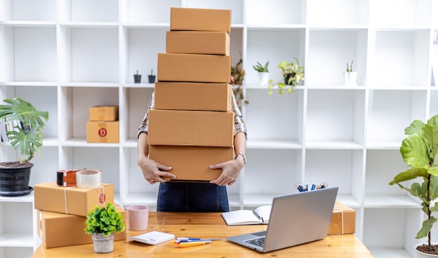 Beautiful Asian woman lifting a bunch of parcels, she owns an online store, she packs and ships through a private transport company. Online selling and online shopping concepts.