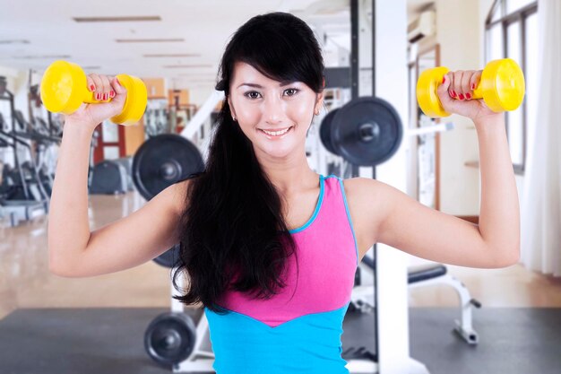 Beautiful Asian woman lifting dumbbells at weights room