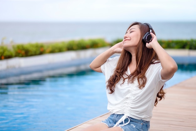 A beautiful asian woman listening to music  with headphone while sitting by swimming pool