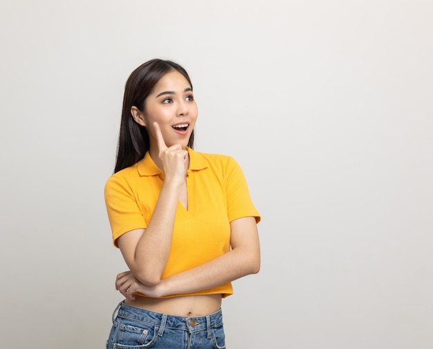 Beautiful asian woman look into blank space. Smiling female wearing yellow shirt on isolated white background. Attractive Teenager girl looking at empty space for text feeling excited and surprised.