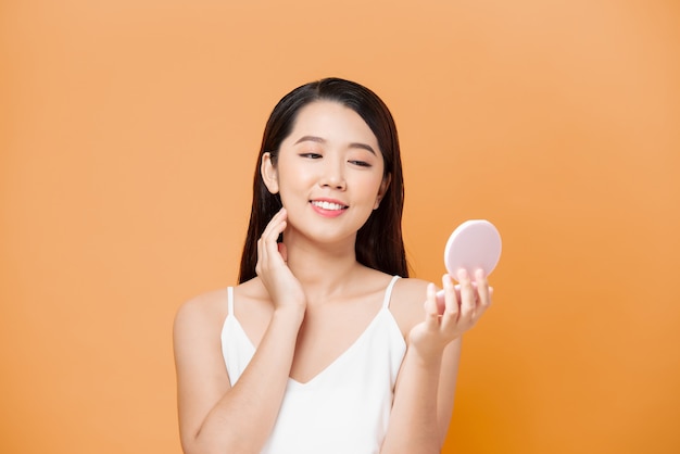 Beautiful asian woman looking her skin in the mirror on yellow background