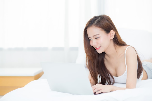 Beautiful asian woman lying on bed using laptop.