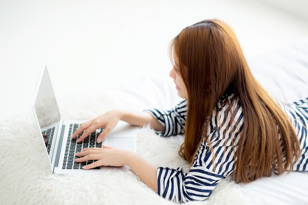 Beautiful asian woman lying on bed using laptop