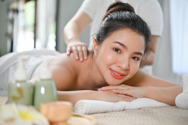 Beautiful Asian woman lying on spa massage table getting back massage by a Thai masseur