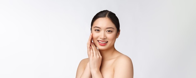 흰색 배경에 격리된 웰빙으로 완벽한 미인의 뺨과 미소 얼굴을 만지는 화장품 소녀의 아름다운 아시아 여성 화장