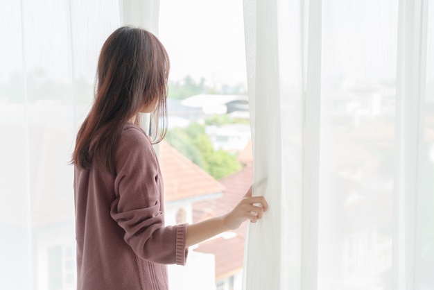 Beautiful asian woman open the curtain in the morning