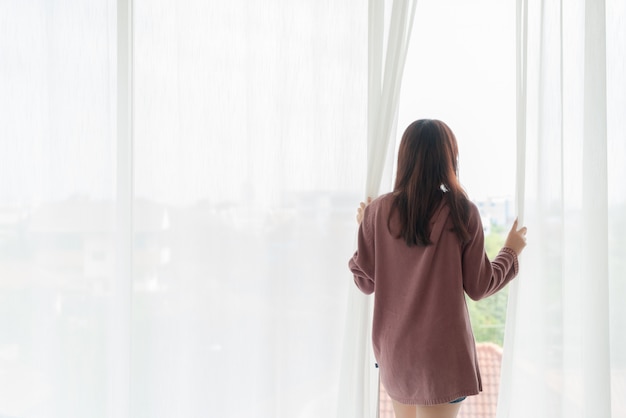 Beautiful asian woman open the curtain in the morning