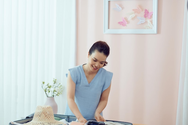 여행 가방에 여름 옷을 포장하는 아름다운 아시아 여성이 웃고 생각을 바라보고 있다