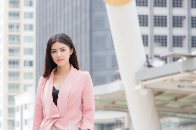 Una bella donna asiatica in un abito rosa è in piedi all'aperto con un grattacielo al mattino a bangkok, in thailandia.