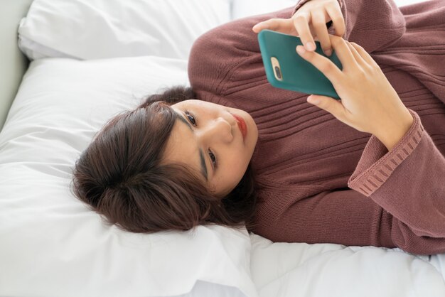 Beautiful asian woman playing smartphone on bed