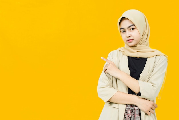 Photo beautiful asian woman pointing hand to empty space on yellow wall