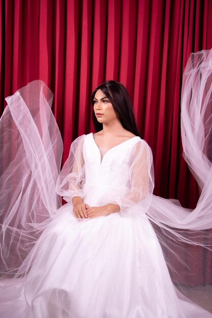 Beautiful Asian woman posing in an expensive wedding dress in front of the red curtain