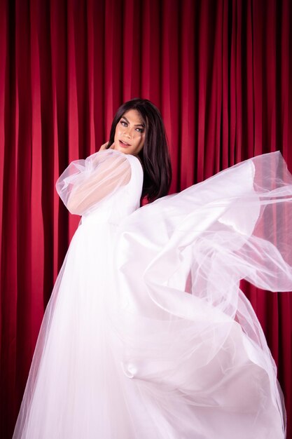 Beautiful Asian woman posing in a flying wedding dress in front of the red curtain