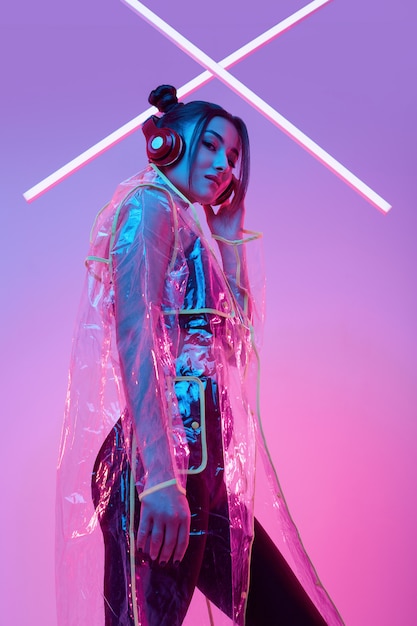 Beautiful asian woman in a raincoat listens music in headphones around colorful neon