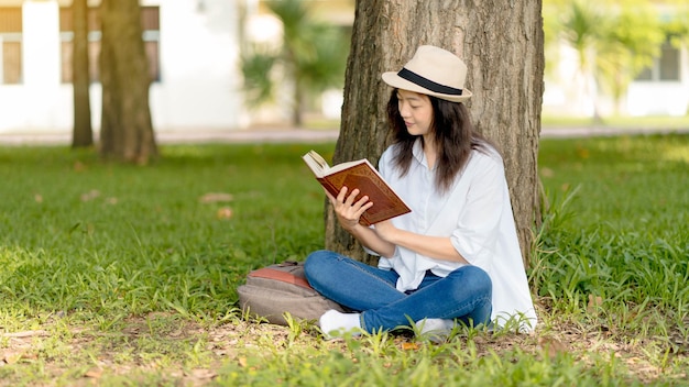 公園で本を読んでいる美しいアジアの女性レクリエーション教育と研究の好奇心余暇の概念