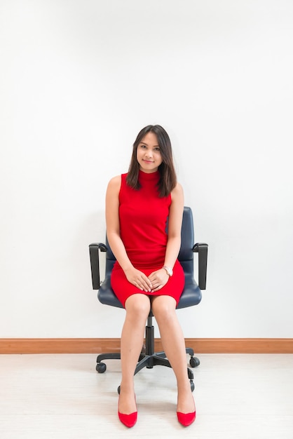 Beautiful asian woman in red dress pose for take a photo on the chair on white wall background