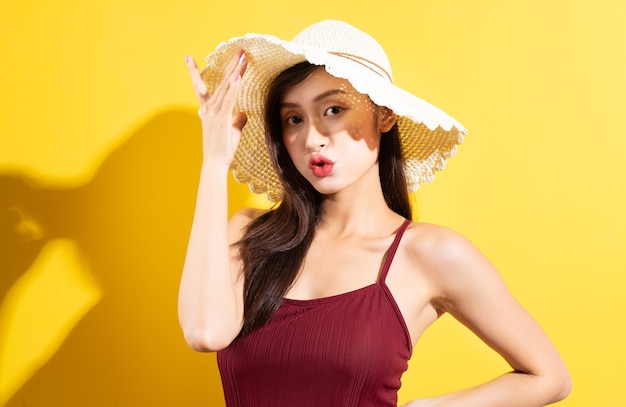 Красивая азиатская женщина в красном купальнике и позирует на желтой стене