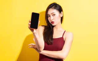 Beautiful asian woman in red swimsuit and using phone on yellow wall